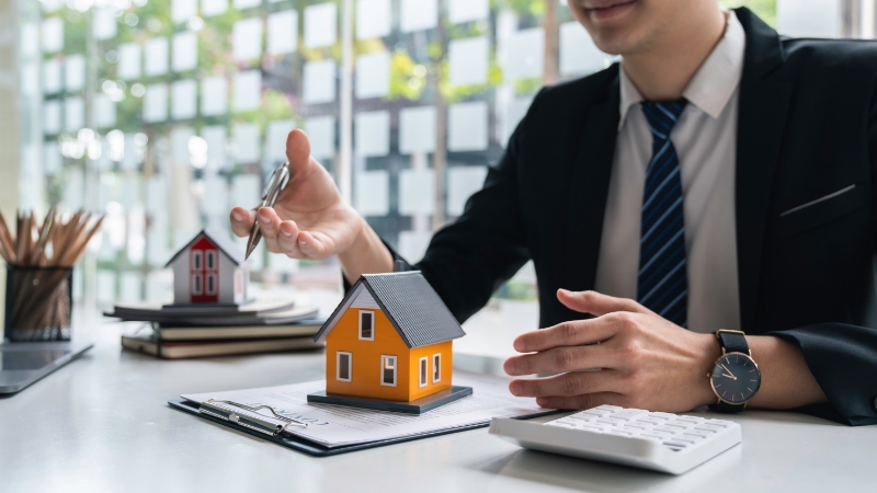 Man in suit explaining home equity using toy houses for visualization.